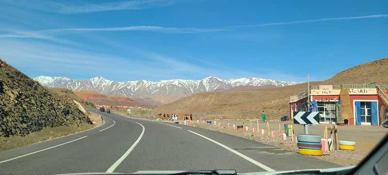 Paved highway winding toward snow-covered Atlas Mountains in Morocco.